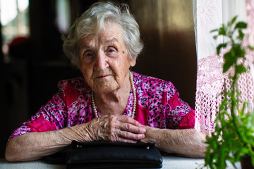 Portrait of an elderly lady with a handbag at the table.