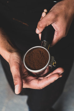 High angle close up of person holding espresso machine portafilter with ground espresso.