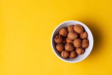 White bowl full of nuts on a yellow background.