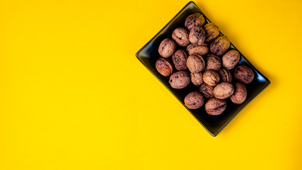 Black plain dish full of nuts on a yellow background.