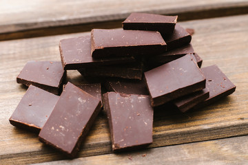 Dark chocolate is lying on a wooden background. Soft focus