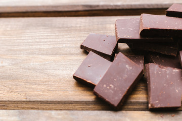 Dark chocolate is lying on a wooden background. Soft focus