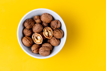 White bowl full of nuts on a yellow background.