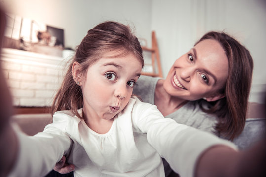 Positive cute girl taking photos with her mom