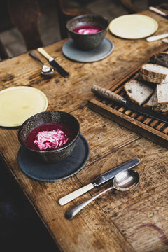 High angle close up of black bowls of beetroot soup and bread on a vintage wooden table.