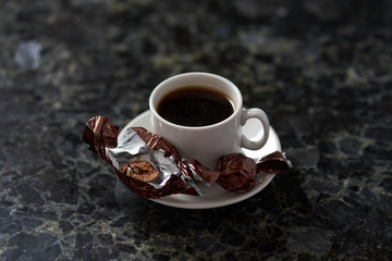 White cup of esoresso with bitten chocolate candy on granite table surface