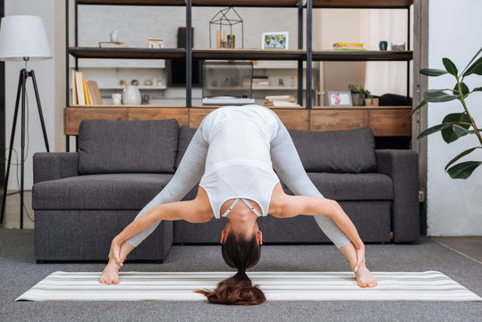 young woman practicing wide legged forward bend pose at home in living room