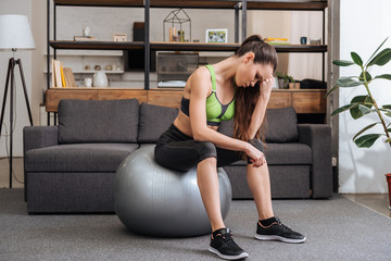 tired sportswoman sitting on fitness ball at home in living room