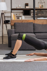 cropped view of sportswoman training with resistance band at home in living room