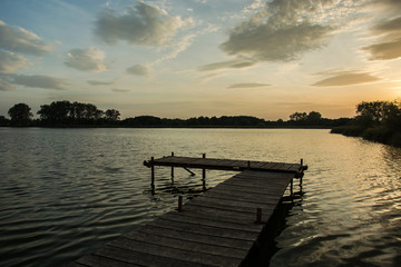 Fototapeta premium Wooden bridge with planks on the lake, trees on the horizon