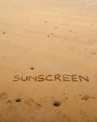 The word sunscreen drawn in sand at the beach with copy space