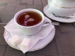 white cup of tea on a saucer with a napkin and pieces of sugar