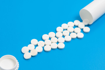 White tablets and bottle for tablets on blue background