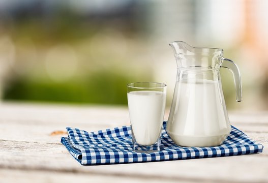 Glass of milk and jar on table with cloth and background