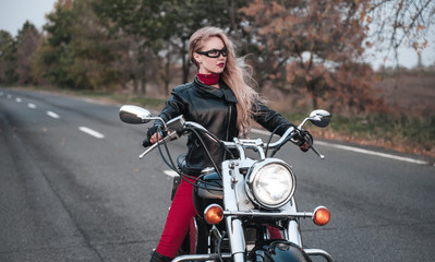 Fototapeta na wymiar Beautiful biker woman posing outdoor with motorcycle on the road. 