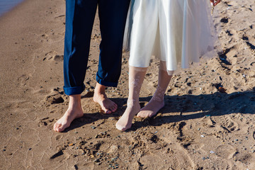 Wedding couple's feet standing on the sandy beach.