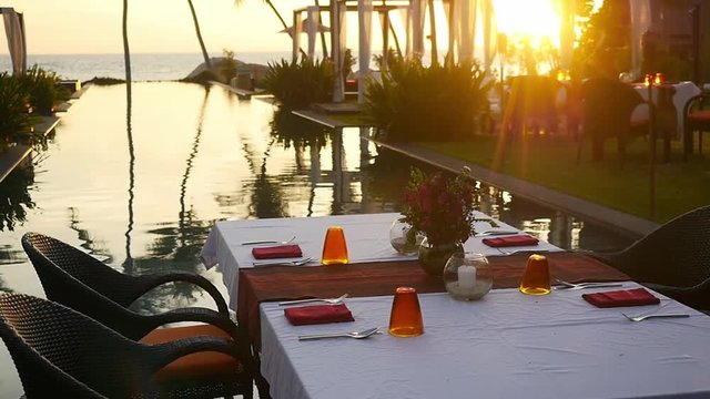 Dining table on tropical island in front of palm trees and swimming pool at amazing sunset. slow motion. 1920x1080