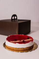 unboxing a cheesecake from its packaging. Cheesecake with red jam with berries and raspberries. On a white table, brown box.