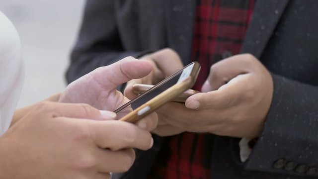 Cropped view of man and woman using cell phones. Close-up partial view of young business people texting via smartphones on street. Connection concept