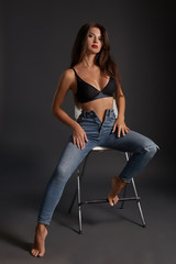 Fototapeta na wymiar Beautiful sexy brunette woman posing in studio, sitting, looking at camera. Girl wearing fashionable jeans and sensual lingerie.
