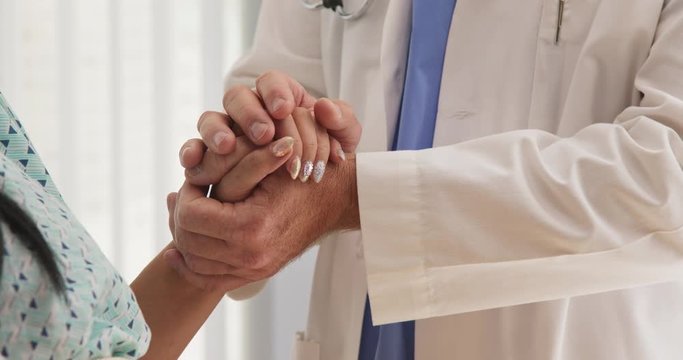 Close up of sympathetic older doctor holding hands of female patient