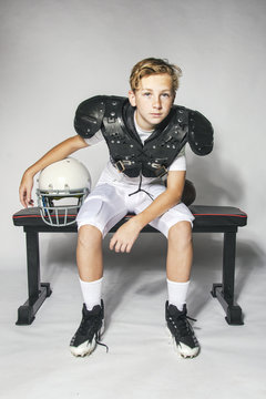Male child football player in shoulder pads relaxing after game