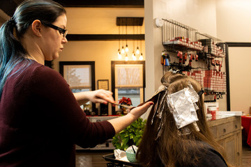 Millennial hair stylist applying highlights in a salon