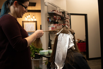 Hair stylist applying hair color to a young brunette woman in a salon