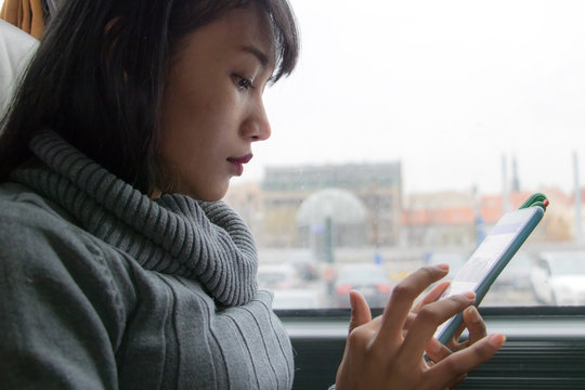 A Young Woman Ride In A Bus. Asian Girl With Mobile Phone Travels In Public Transport. A Bus Passenger Uses A Mobile Phone.