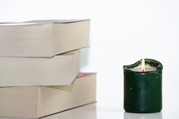 Composition of green burning candle and pile of books against white background