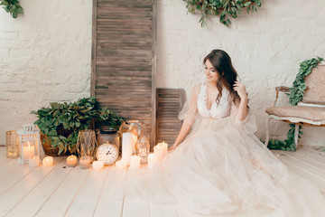 A girl in a beige peignoir, with a wreath of flowers on her head, poses in the studio loft, fine...