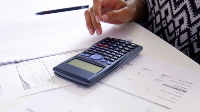 Women hand using a Scientific Calculator close up, with exam preparation papers on the table. School and university study, maths and physics concept.
