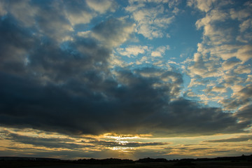 Fototapeta na wymiar Sunset piercing through gray evening clouds in the blue sky