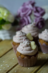 Chocolate muffins with cream sprinkled with hearts. Muffins with icing with flowers in the background. Romantic surprise. Breakfast on the St. Valentine's day