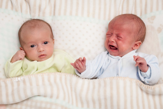 Two adorable twin babies.  One looking, one crying