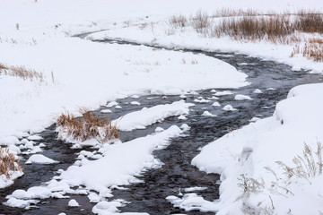 stream flowing among snow at winter day 