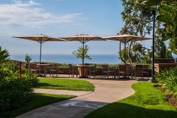 Patio with three tables with umbrellas. There is a stone wall. Patio overlooks the ocean