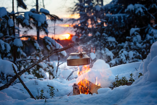 Fireplace and coffee pot in Finland. There is a sunset in the background. There is a lot of snow and frost.