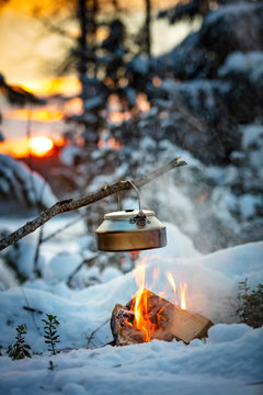 Fireplace and coffee pot in Finland. There is a sunset in the background. There is a lot of snow and frost.