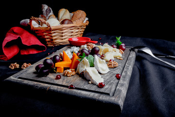 Cheese plate served with grapes, honey and nuts on a wooden background. Various types of cheese