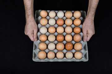 Male hands holding a cardboard egg box full of hen eggs on black mat background