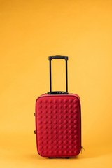 red travel bag with wheels on yellow background