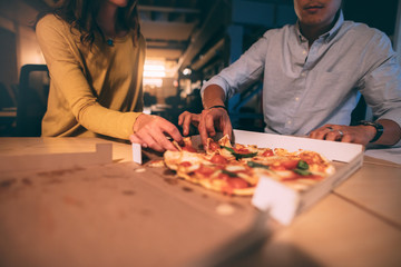 Man and woman eating pizza in office at night