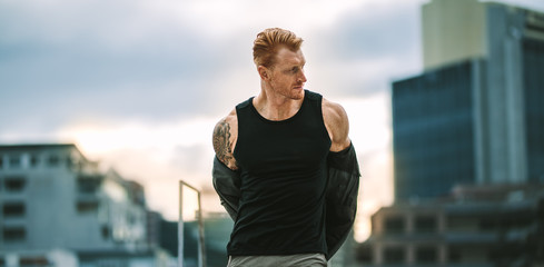 Portrait of a fitness man standing on rooftop removing his shirt