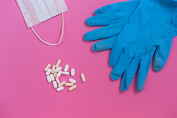 on the pink surface are blue medical gloves, a protective face mask and tablets