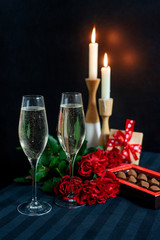 Two glasses with champagne and a bouquet of red roses and candies on the background of candles