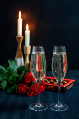 Two glasses with champagne and a bouquet of red roses and candies on the background of candles
