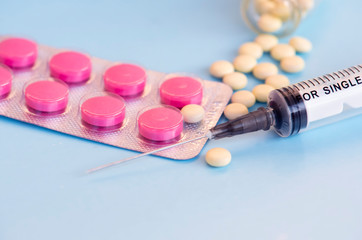 Pills and medical syringe on the blue background .
