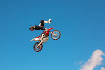 Fototapeta na wymiar Racer on motorcycle participates in motocross cross-country in flight, jumps and takes off on springboard against sky. Concept active extreme rest.