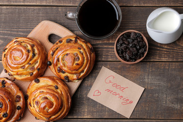 Tasty buns with raisins and coffee with milk on a brown wooden background. fresh bakery. breakfast. view from above